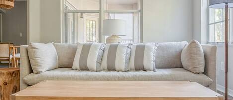 Un sofá de tonos neutros con cojines a rayas, una mesa de centro de madera y una alfombra tejida.