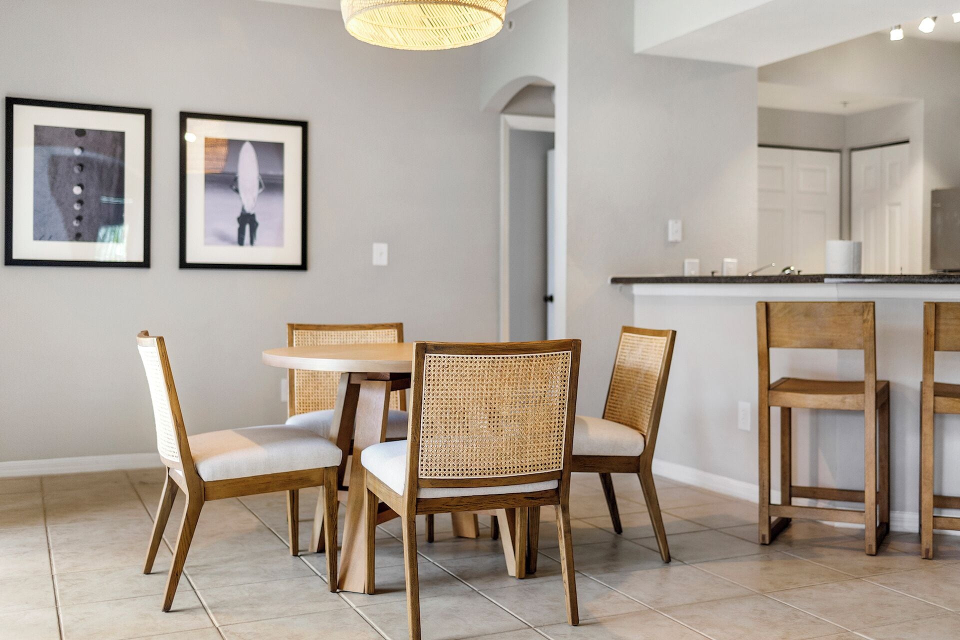 Un coin repas avec une table ronde et quatre chaises, un espace cuisine avec un comptoir et des placards, et deux tableaux encadrés accrochés au mur.