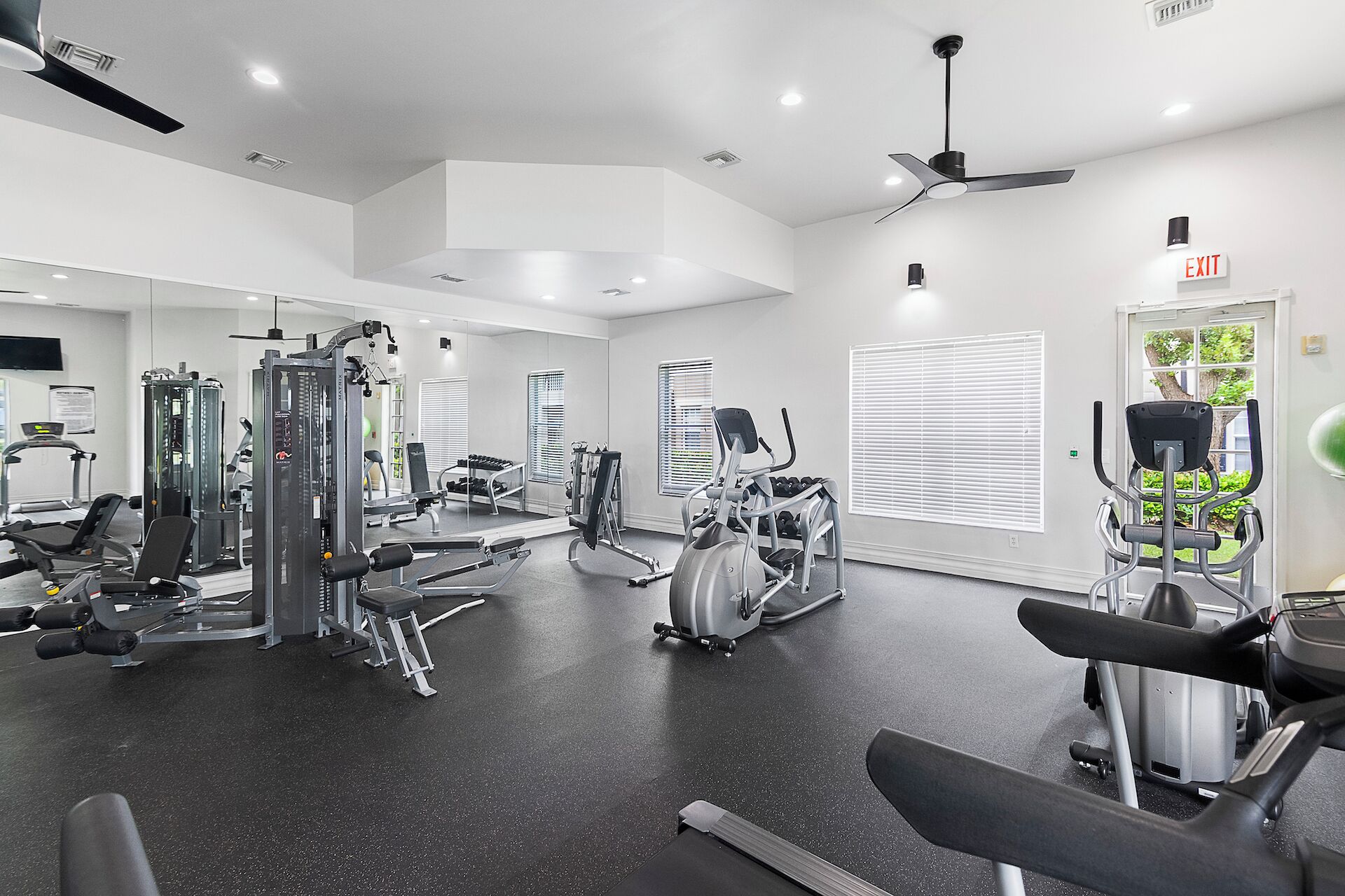 Une salle de sport moderne équipée de divers appareils d’exercice, d’un ventilateur de plafond et d’une porte portant l’inscription « SORTIE ».