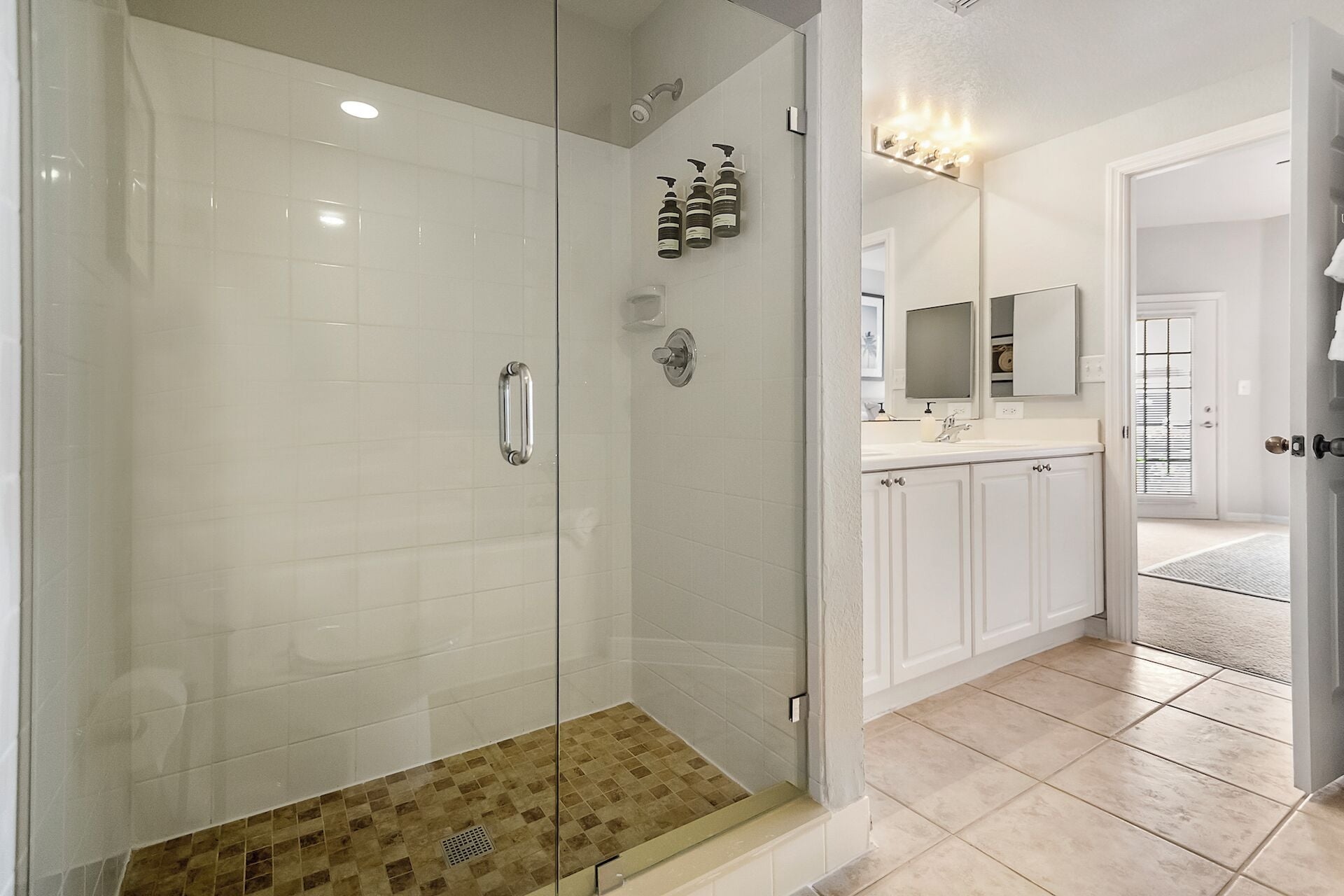 Un baño moderno con ducha envuelta en vidrio, azulejos blancos y un mueble de tocador con espejo y lavabo.