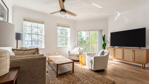 Amplia sala de estar con ventilador de techo, ventanas grandes, televisor de pantalla plana y un mueble de madera.