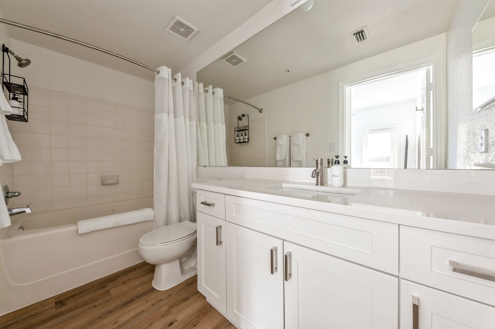 Un baño moderno con bañera, inodoro y tocador con un espejo grande.
