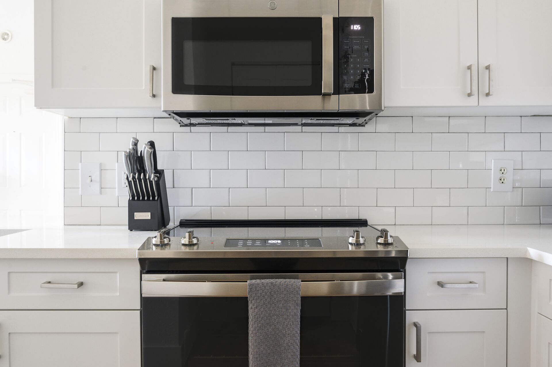 A modern kitchen with a stainless steel microwave, oven, and a knife block on the countertop.