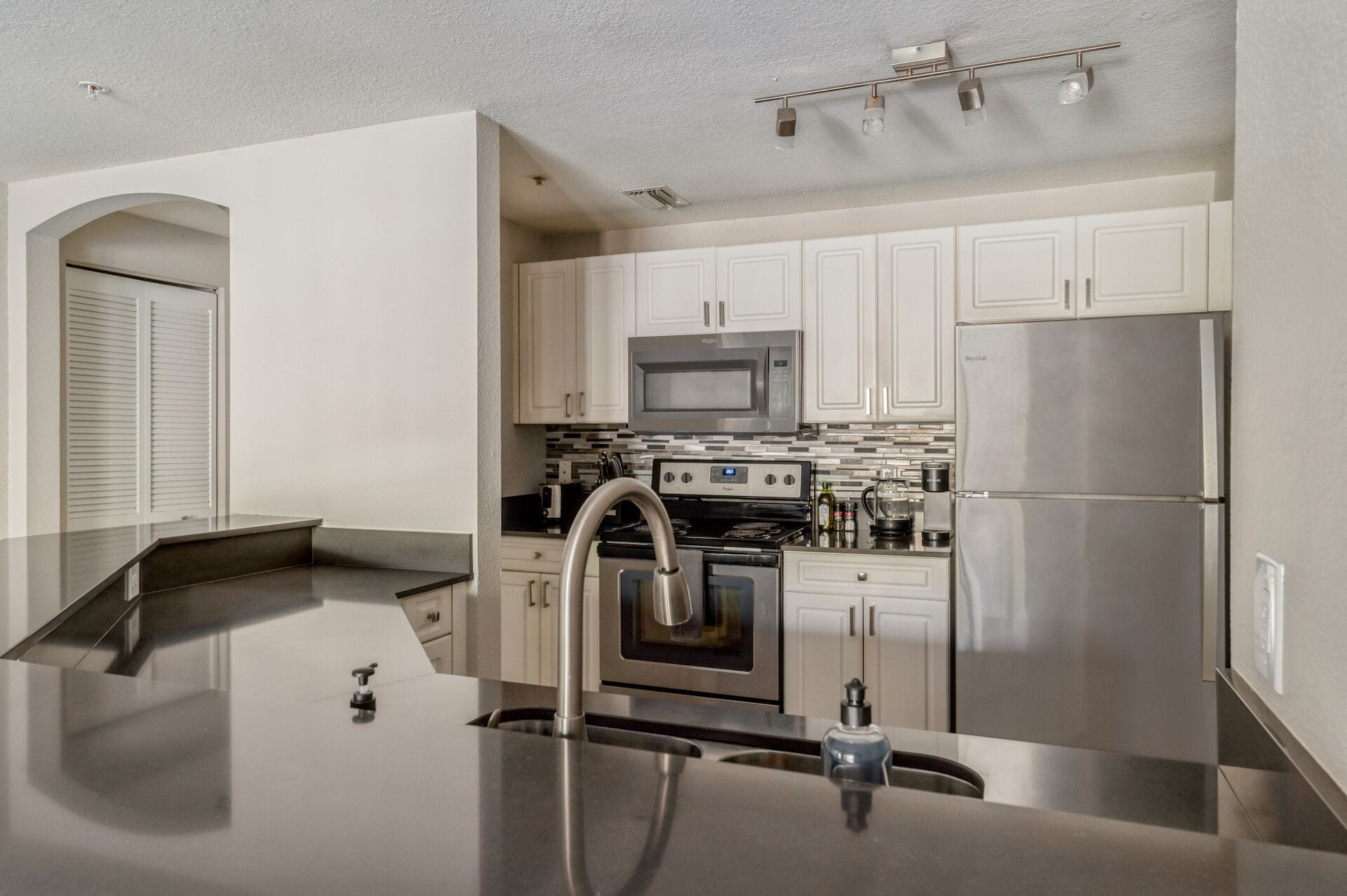 Una cocina moderna con electrodomésticos de acero inoxidable, armarios blancos y una encimera elegante.