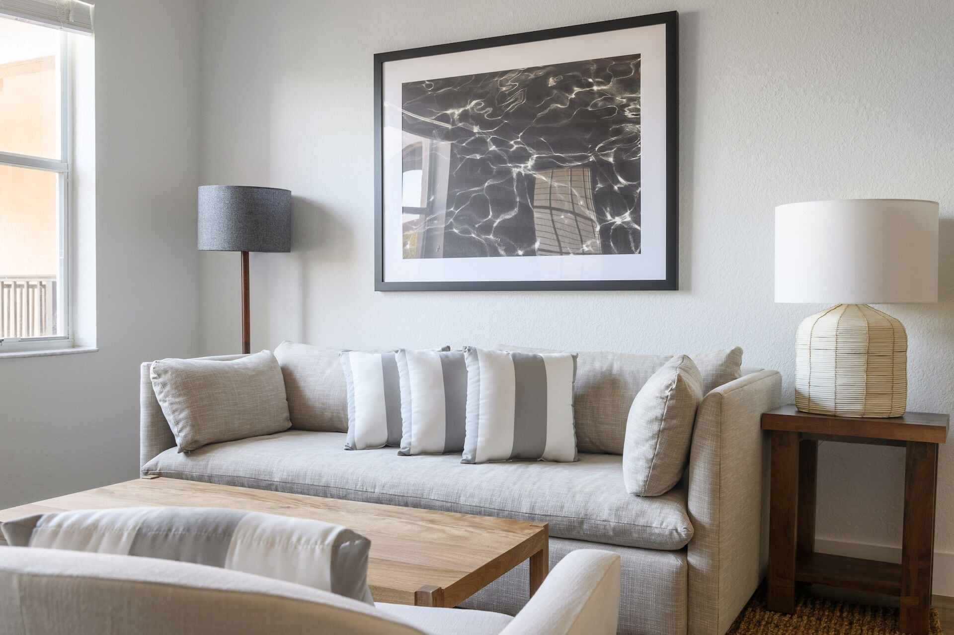 A modern living room with a grey sofa, striped pillows, a wooden coffee table, and a framed artwork on the wall.
