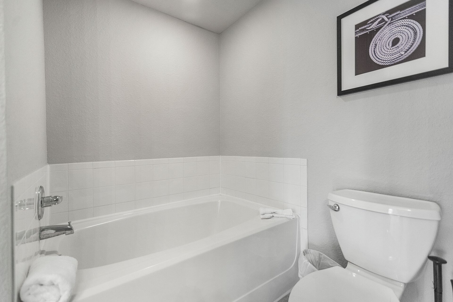 Ein Badezimmer mit einer weißen Badewanne, einer Toilette und einem gerahmten Bild an der Wand.