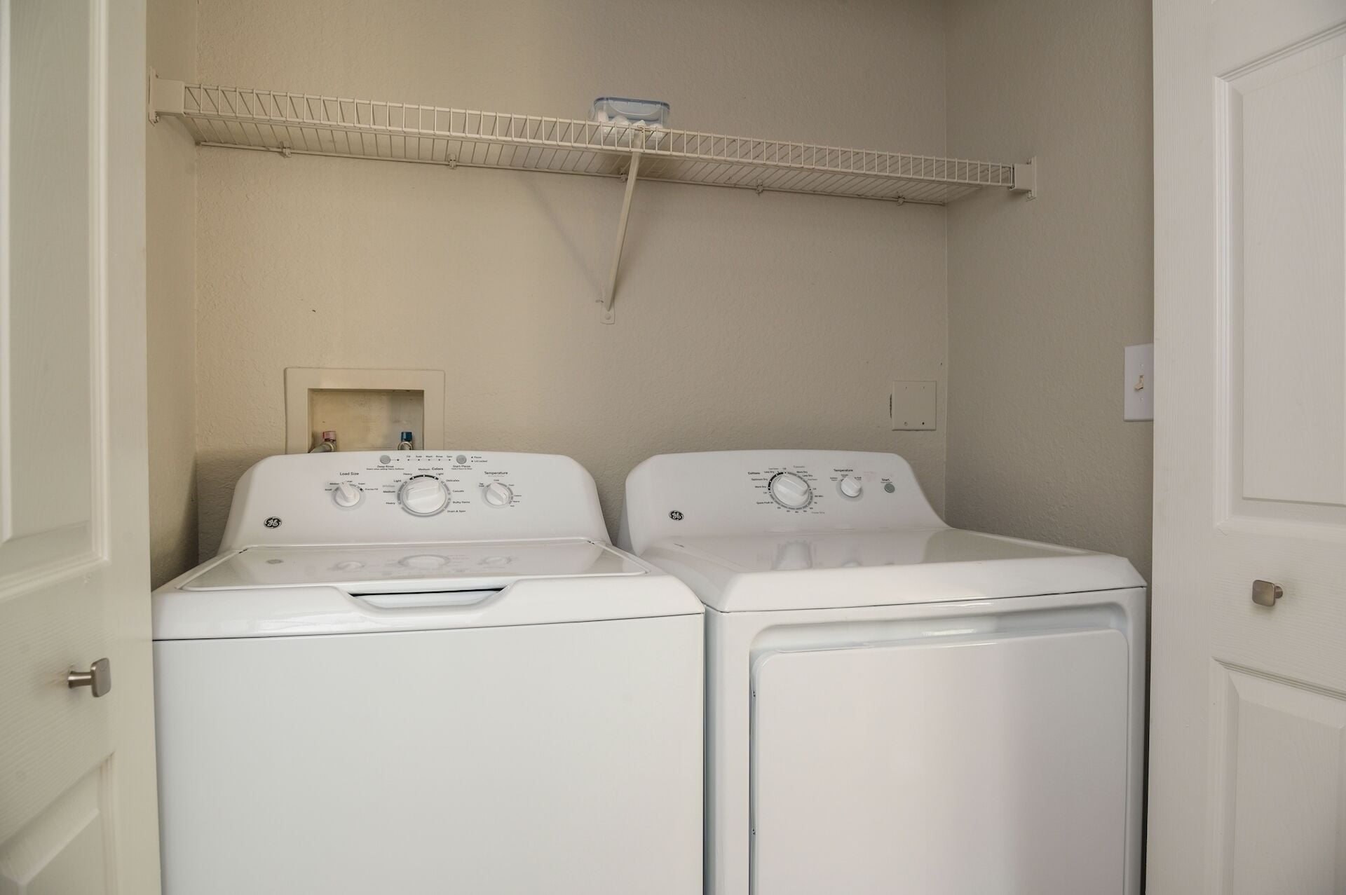 A laundry room with two front-loading washers and a shelf above them.