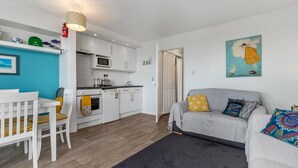 Un espacio habitable compacto con kitchenette, comedor y sofá con cojines coloridos.