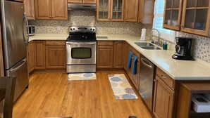 A kitchen with wooden cabinets, stainless steel appliances, a tiled backsplash, and a window with blinds.