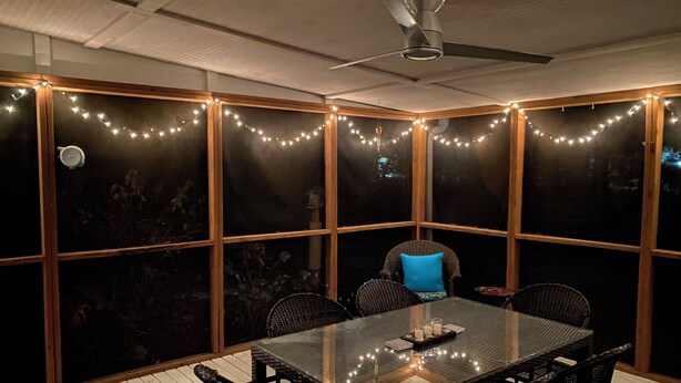 A dining area with a glass table, black chairs, and a ceiling fan.