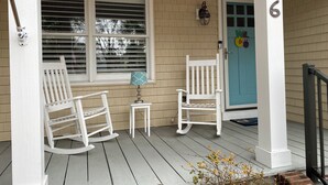 A porch with two rocking chairs, a small table, and a blue door.