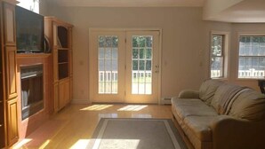 A living room with a sofa, a television on a wooden stand, and a sliding glass door leading to an outdoor area. - Centrally Located Cape (Lee)