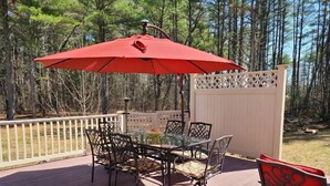 A deck with a glass table and chairs, a red umbrella, and a white fence. - Centrally Located Cape (Lee)