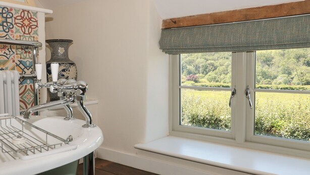 A bathroom with a sink, a window with a view of a garden, and a decorative vase.
