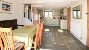 A spacious dining area with a high ceiling, a staircase leading to an upper level, and a kitchen with a view.