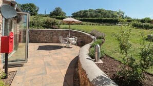 A patio area with a stone wall, outdoor seating, and a view of a landscaped garden.