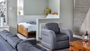 A modern bedroom with a bed, a grey armchair, a wooden dresser, and a small table with glasses and a bottle. - The Martlet Inn (Wellington)