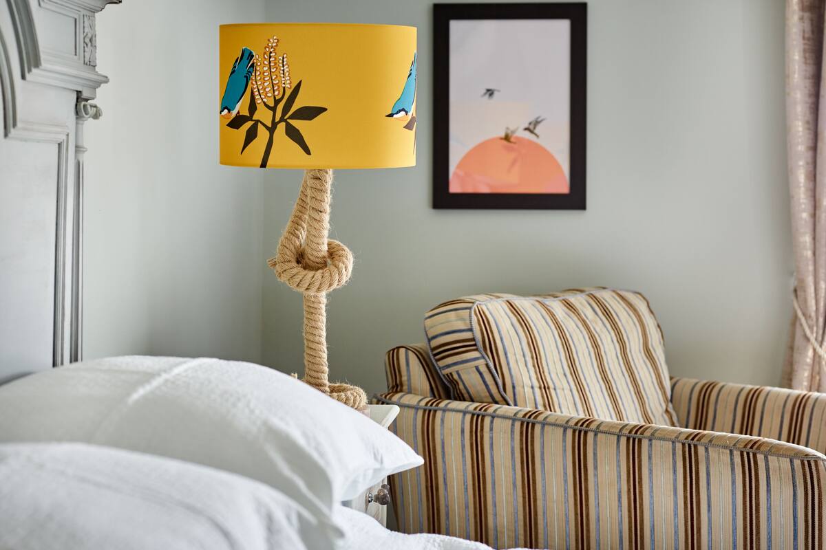A room with a bed, a striped armchair, a rope chandelier, and a framed picture on the wall.