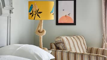 A room with a bed, a striped armchair, a rope chandelier, and a framed picture on the wall.