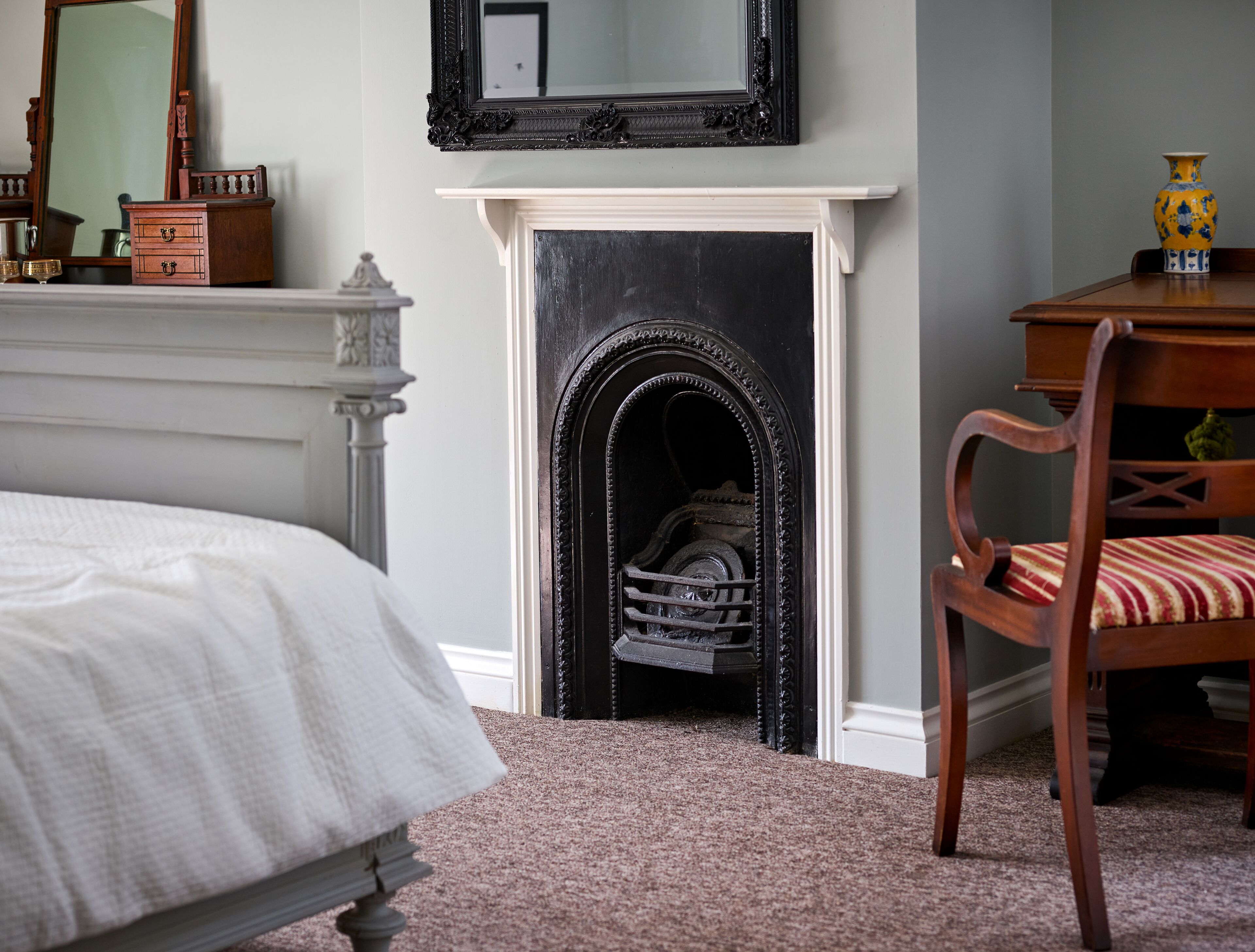 A bedroom with a bed, a fireplace, a chair, and a dresser.