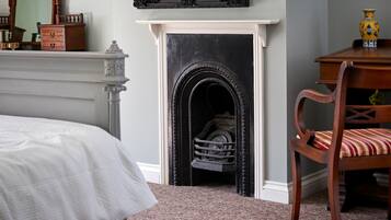 A bedroom with a bed, a fireplace, a chair, and a dresser.