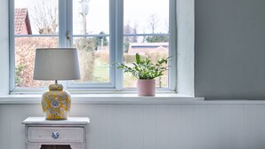 A bedroom with a bed, a bedside table with a lamp, a potted plant, and a window with a view of the outside. - The Martlet Inn (Wellington)