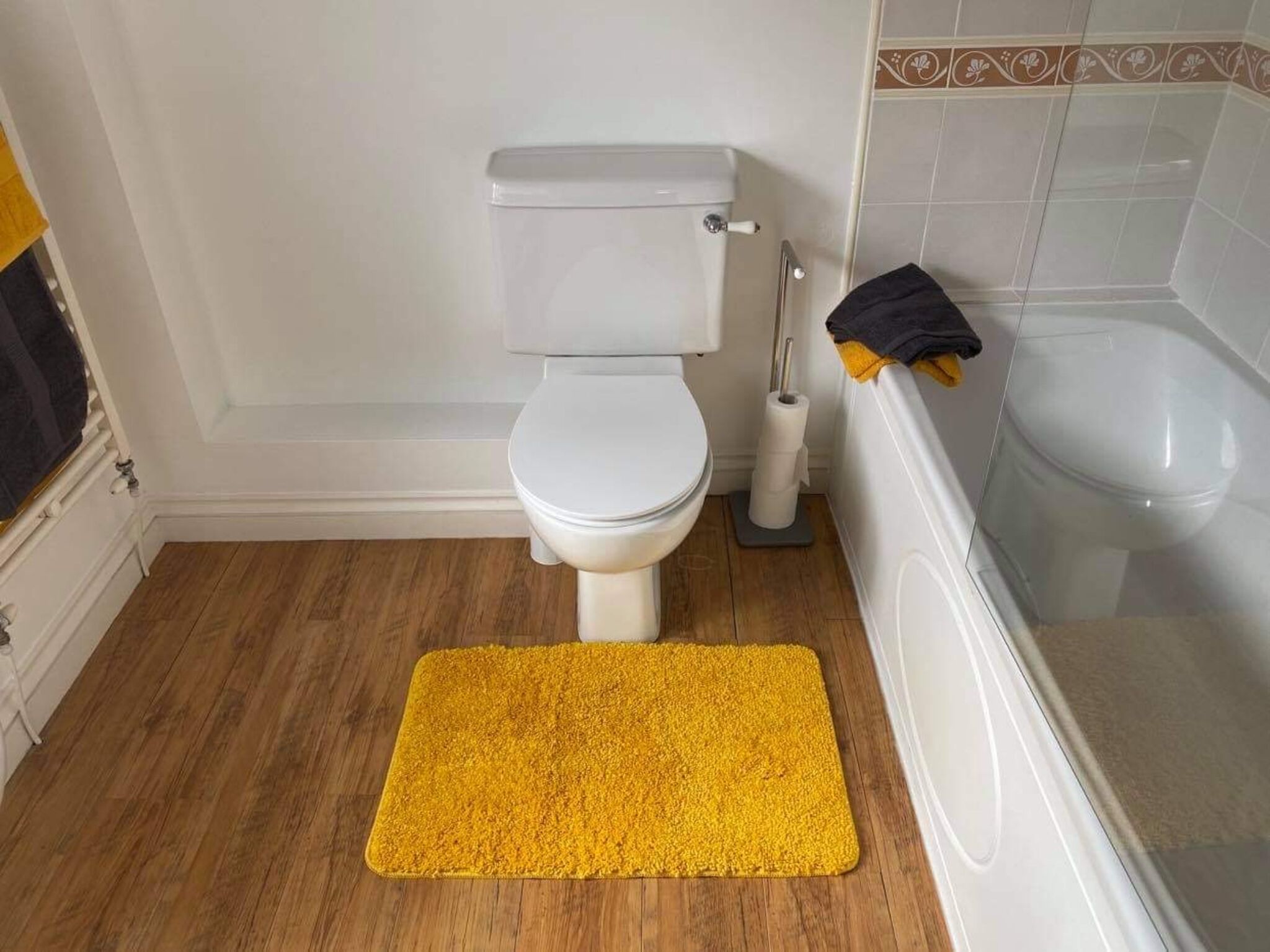 A bathroom with a toilet, a yellow bath mat, and a bathtub.