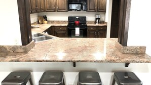 A kitchen with granite countertops, dark wooden cabinets, a stainless steel sink, a microwave, a stove, and a coffee maker. There are three stools in front of the counter. - Pet-friendly 5 bed/4 bath home, just minutes to Beaver Creek, Avon, and Vail (Avon)