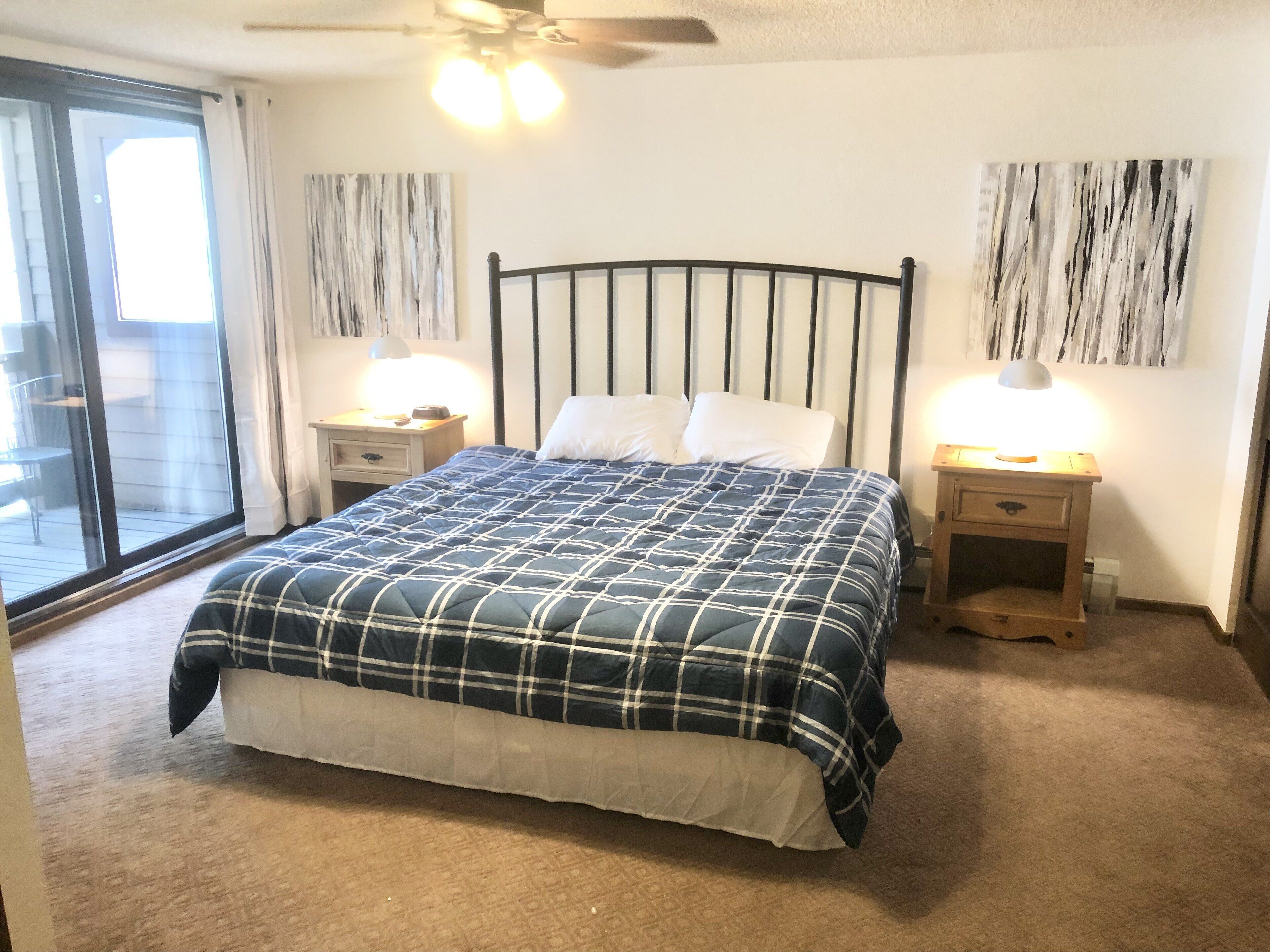 A bedroom with a bed, two bedside tables, a ceiling fan, and a view through a sliding glass door.
