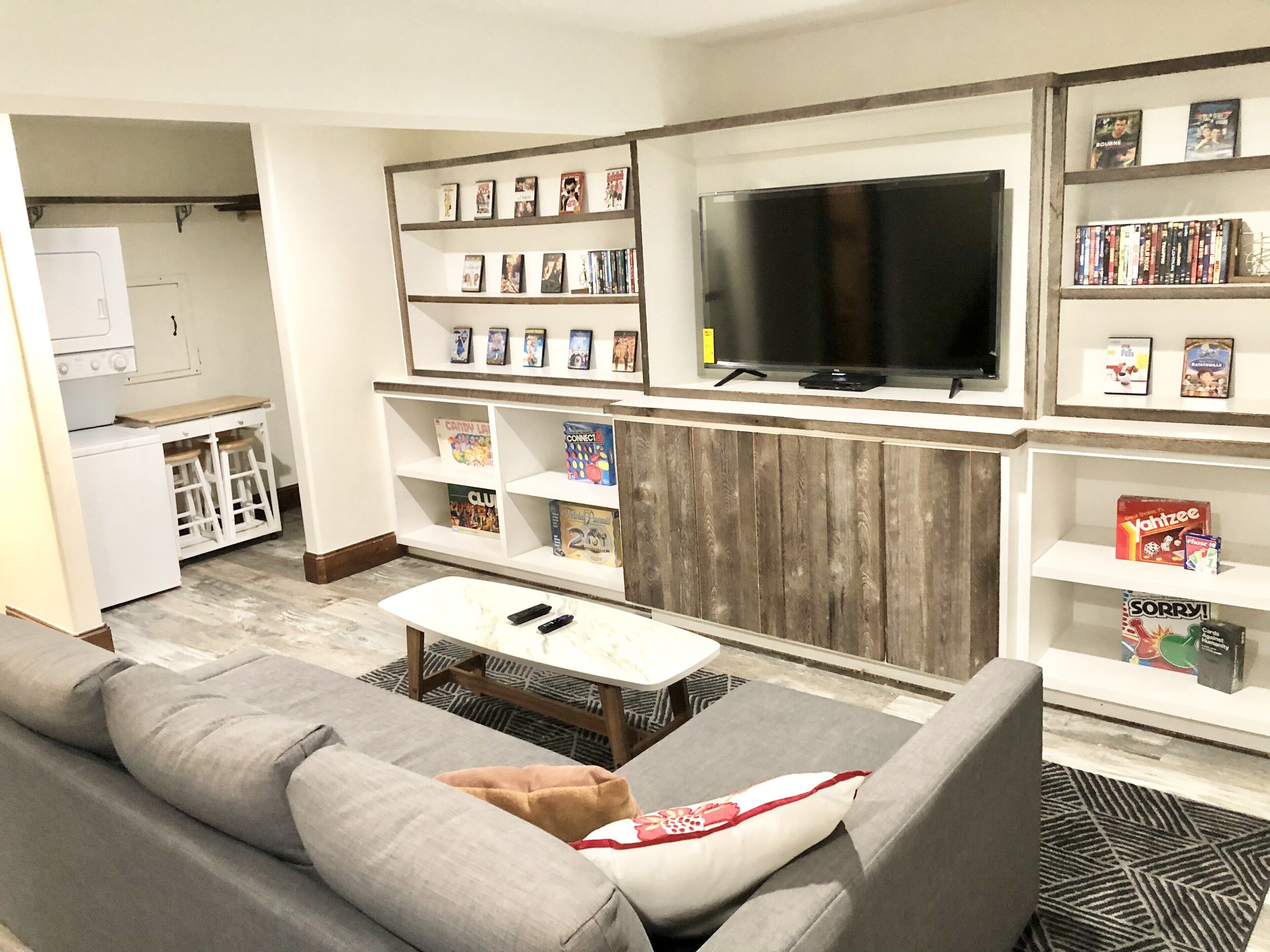 A modern living room with a grey sofa, a coffee table, a TV, and built-in shelves with books and decorations.