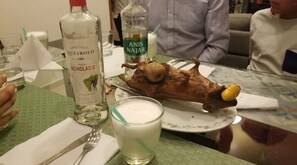 Uma mesa de jantar com um leitão assado, uma garrafa de Santiago Queirolo e um copo de leite.