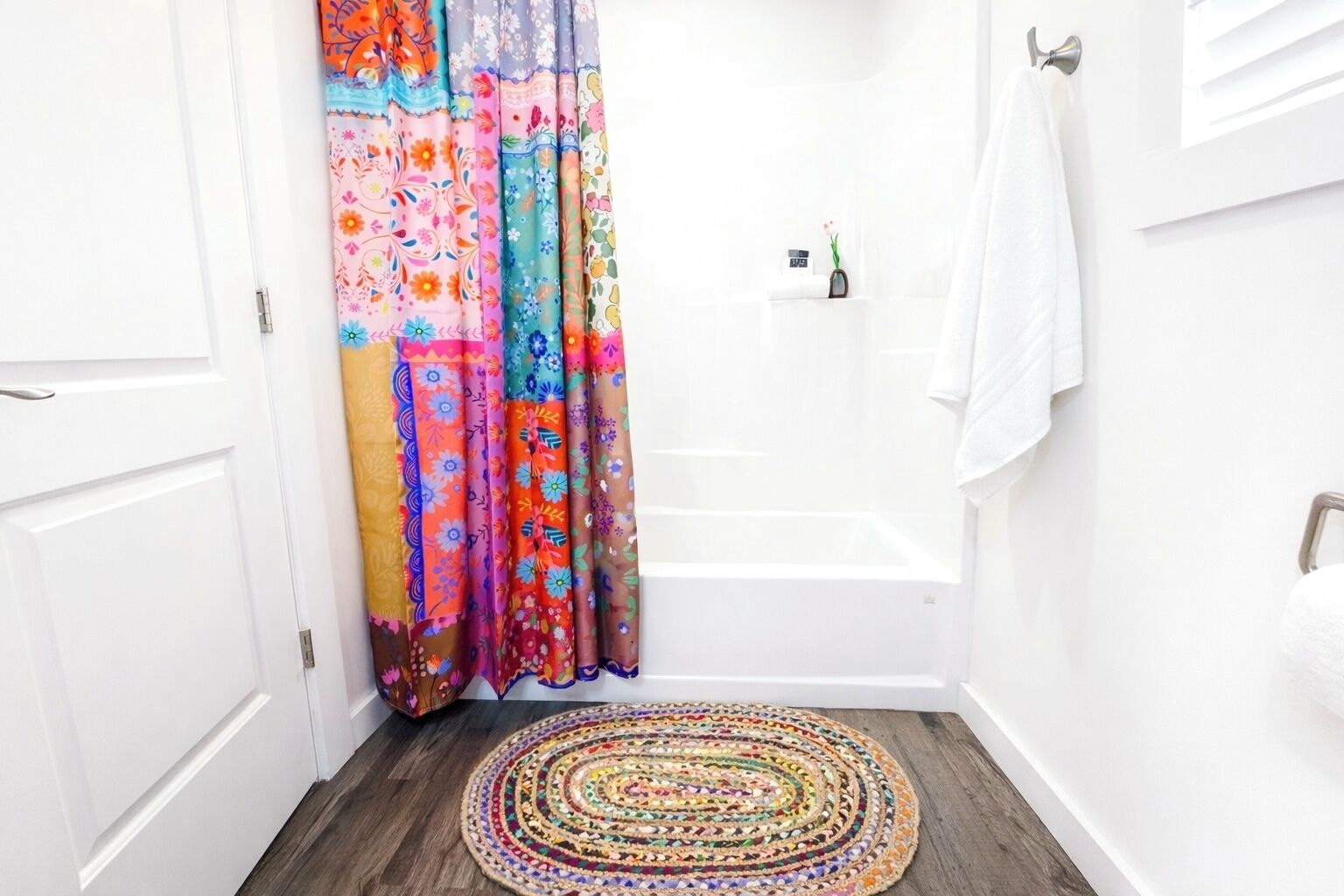 Une salle de bain avec une baignoire blanche, un rideau de douche coloré et un tapis à motifs sur le sol.