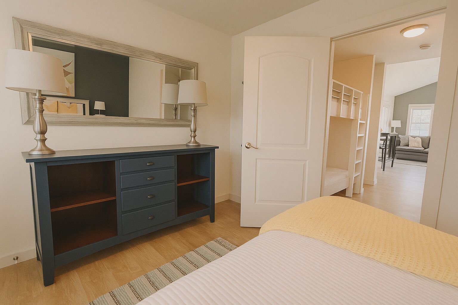 Un dormitorio con cama, cómoda con lámparas, espejo y puerta que da a un pasillo.
