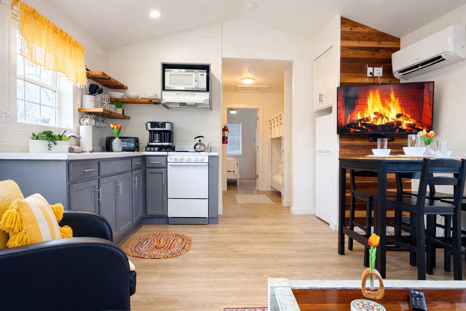 A modern kitchen with a built-in microwave, stove, and oven. There is a dining area with a table and chairs, and a living room with a sofa and a coffee table.
