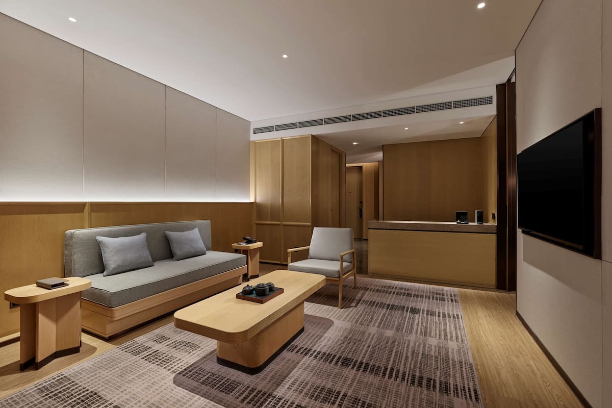 A modern hotel room with a sofa, armchair, coffee table, and a TV.