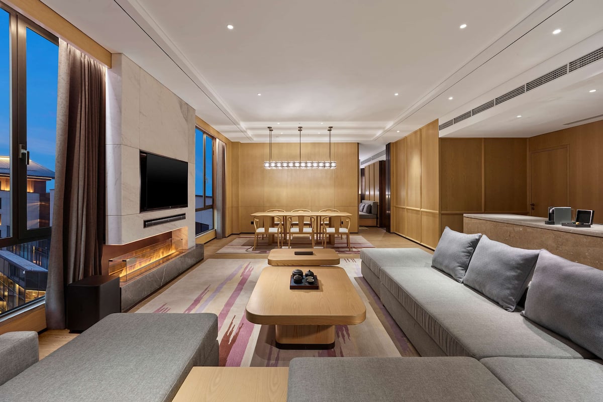 A modern living room with a large sofa, a TV, a fireplace, a dining area, and a view of the city.
