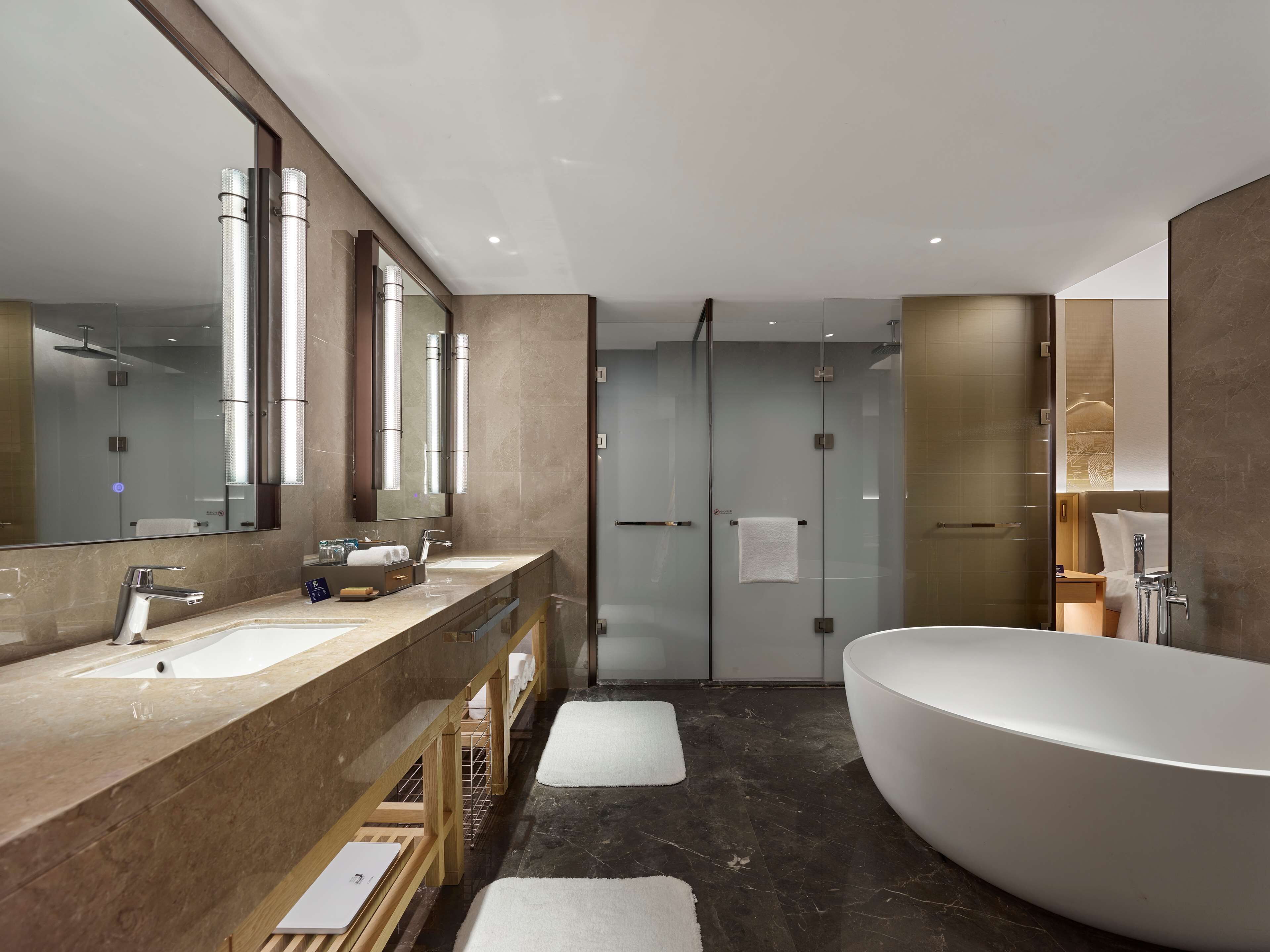 Un baño moderno con una bañera grande, una ducha con cerramiento de vidrio y un tocador con espejo y varios lavamanos.