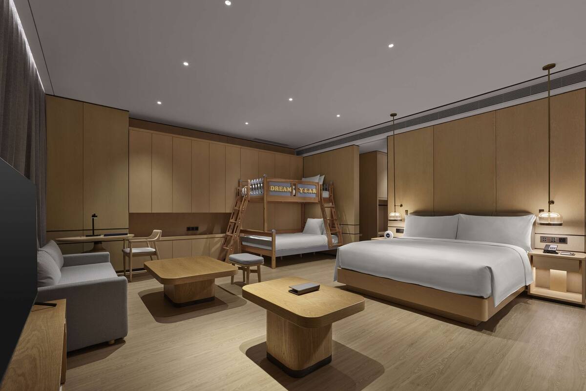 A modern hotel room with a large bed, two seating areas, a desk, and a ladder leading to a bunk bed.