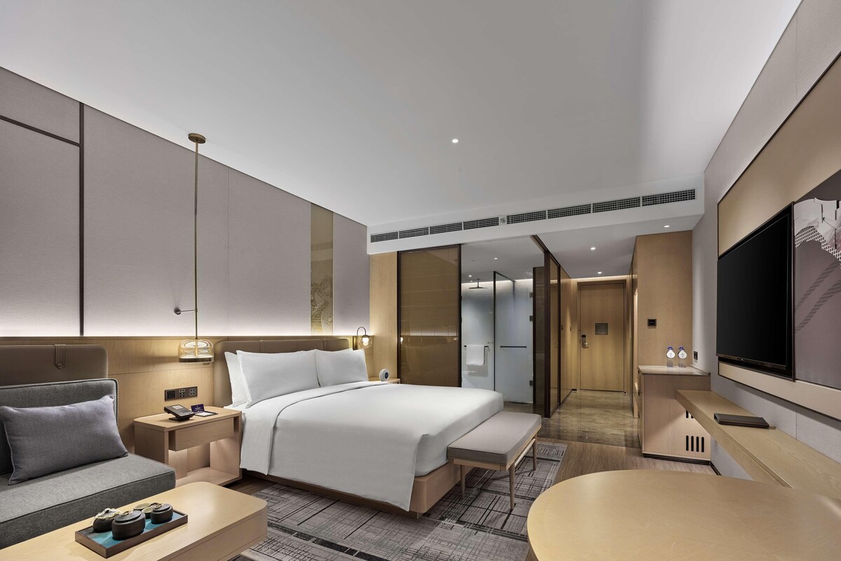 A modern hotel room with a large bed, bedside tables, a sofa, a desk, and a TV.