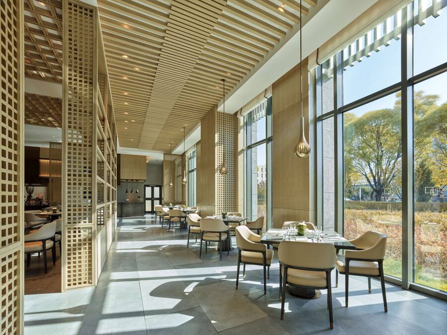 A modern dining area with high ceilings, large windows, and a view of the outdoors.