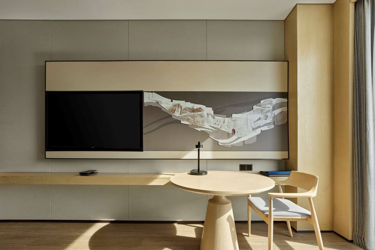 A modern room with a large flat-screen TV mounted on the wall, a round wooden table with a chair, and a wooden floor.