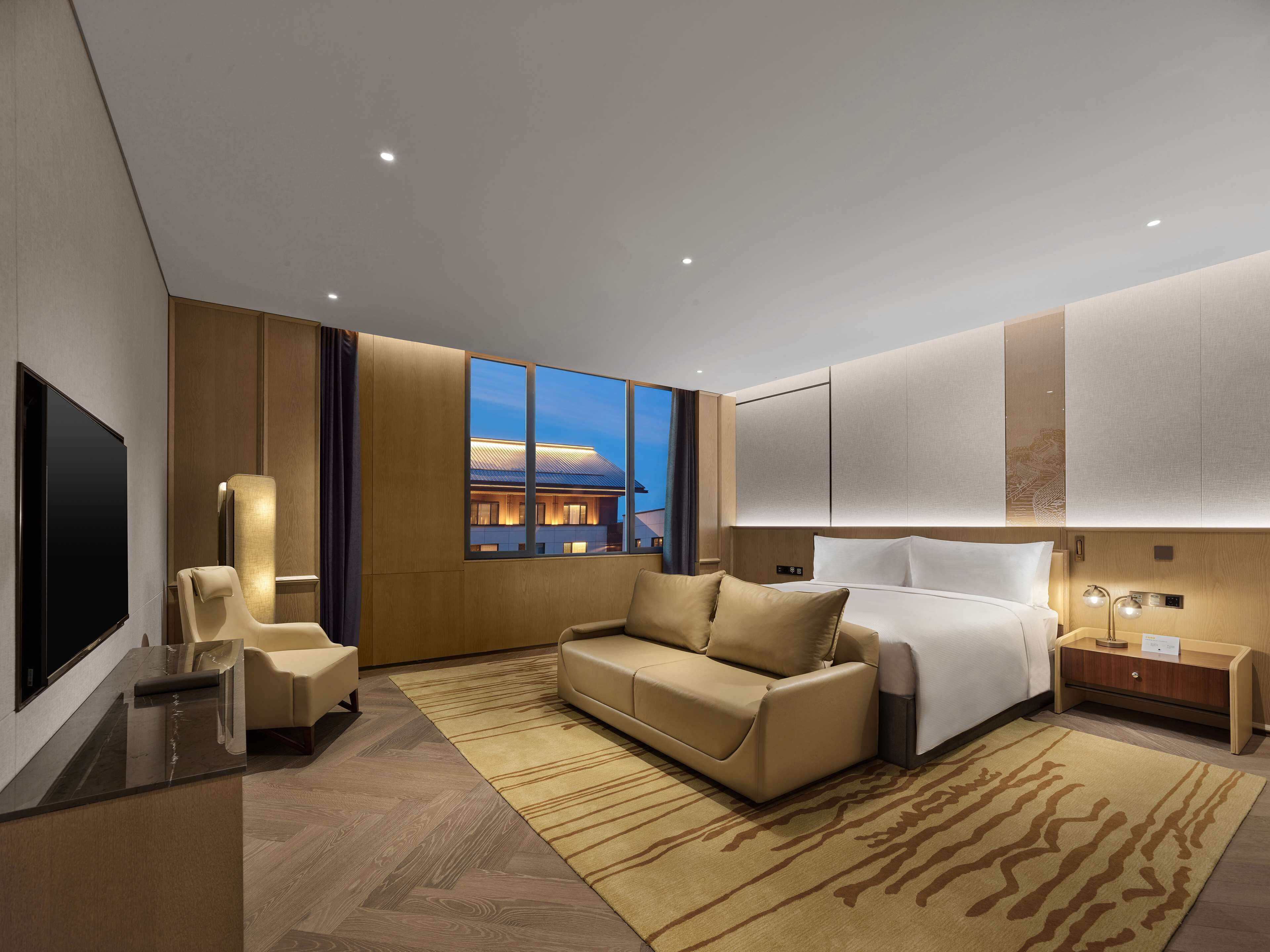 Une chambre d’hôtel moderne avec un grand lit, un canapé, une télévision et une vue sur un bâtiment à l’extérieur.