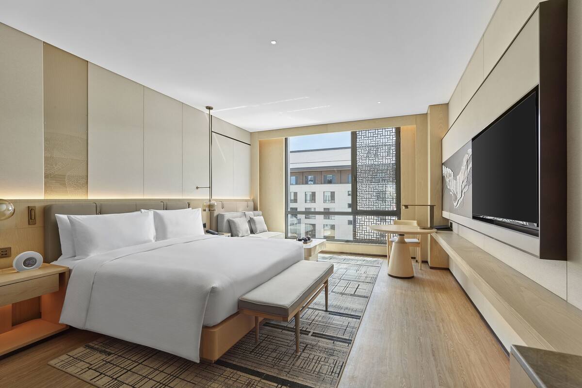 A modern hotel room with a large bed, a flat-screen TV, and a view of the city.