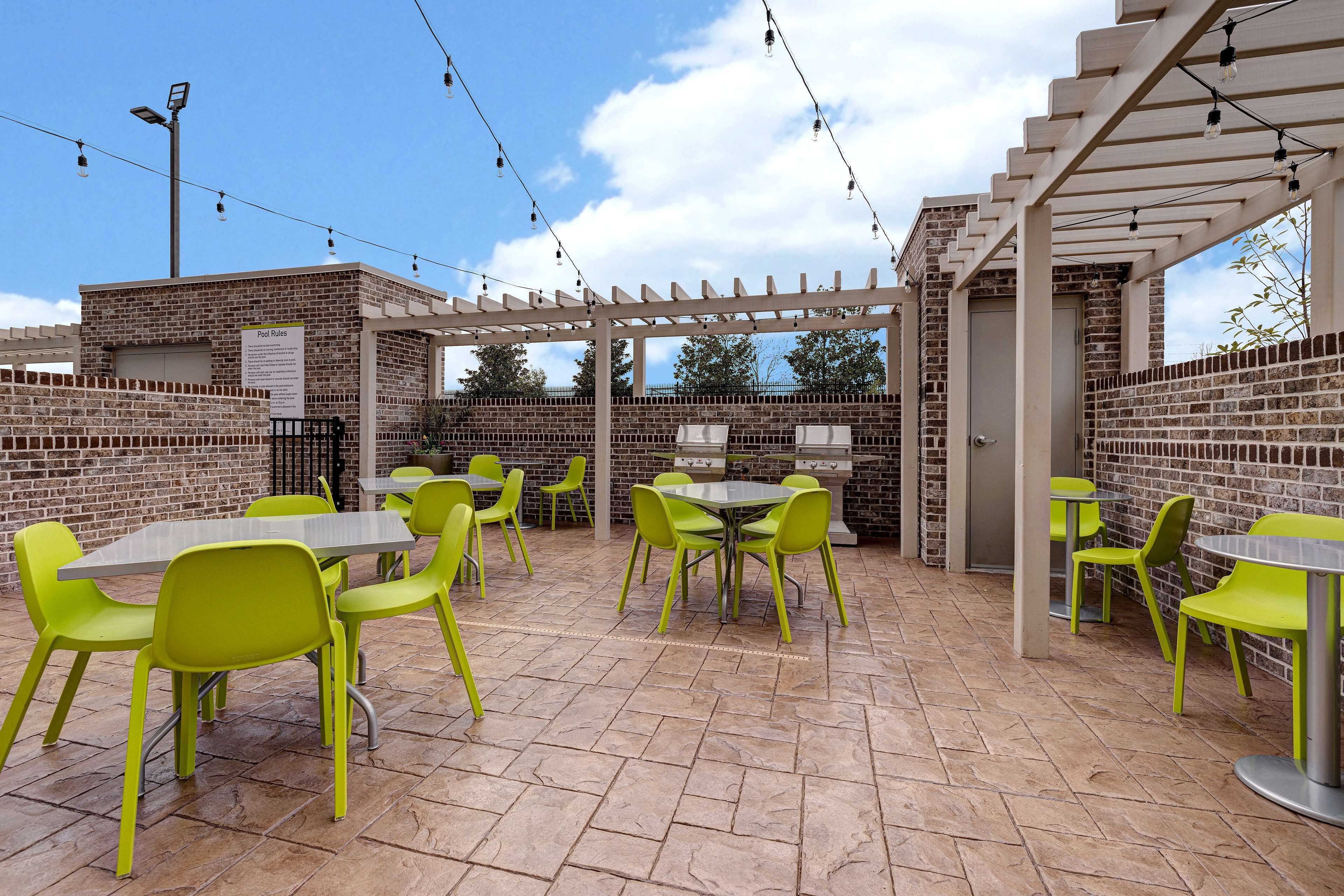 An outdoor patio with brick walls, green chairs, and tables.