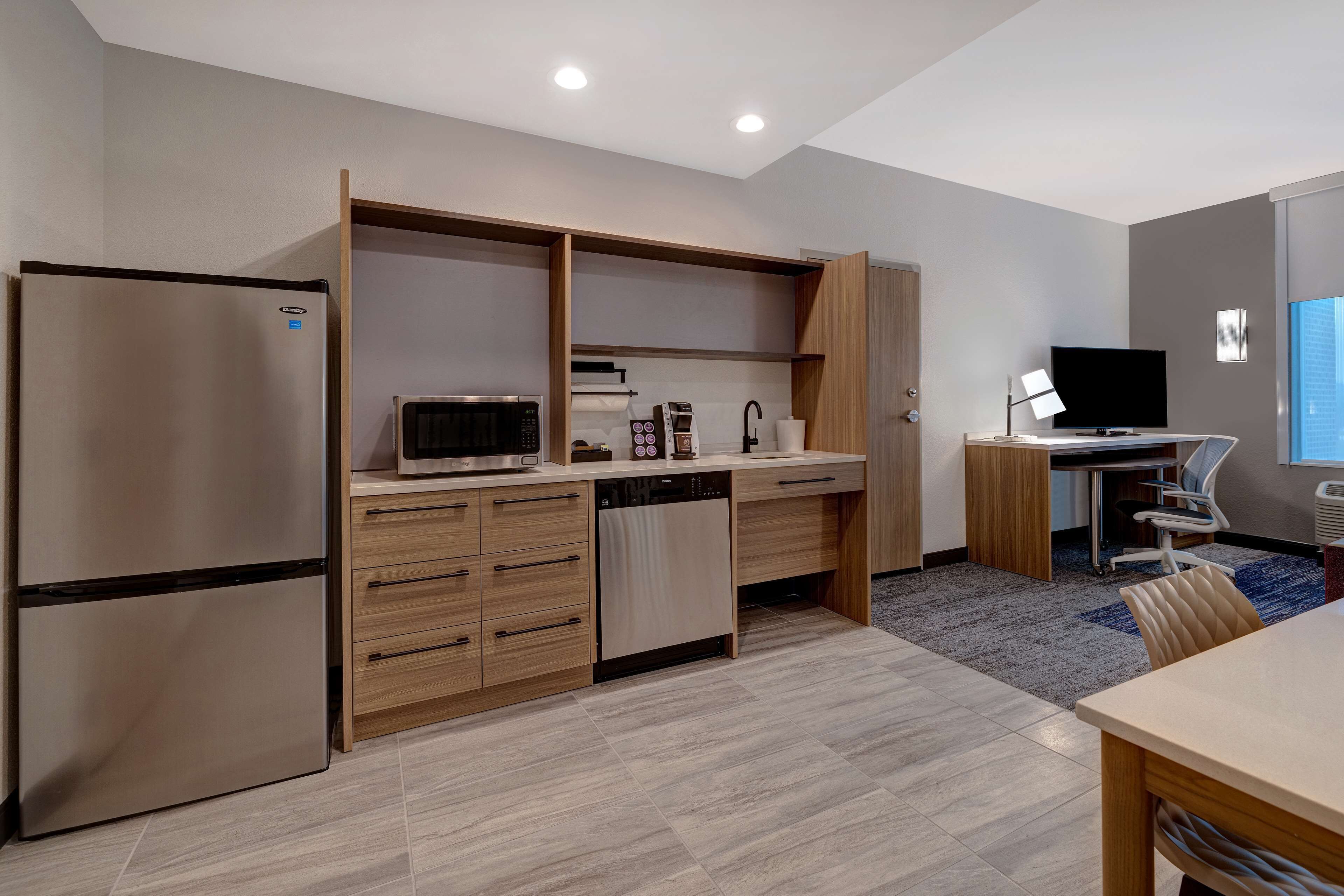 A modern kitchen with a built-in refrigerator, microwave, and dishwasher, a wooden countertop, and a desk with a computer and chair.