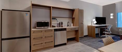 A modern kitchen with a built-in refrigerator, microwave, and dishwasher, a wooden countertop, and a desk with a computer and chair.