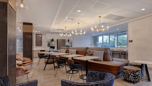 A modern lounge area with seating arrangements, tables, and a kitchen in the background.