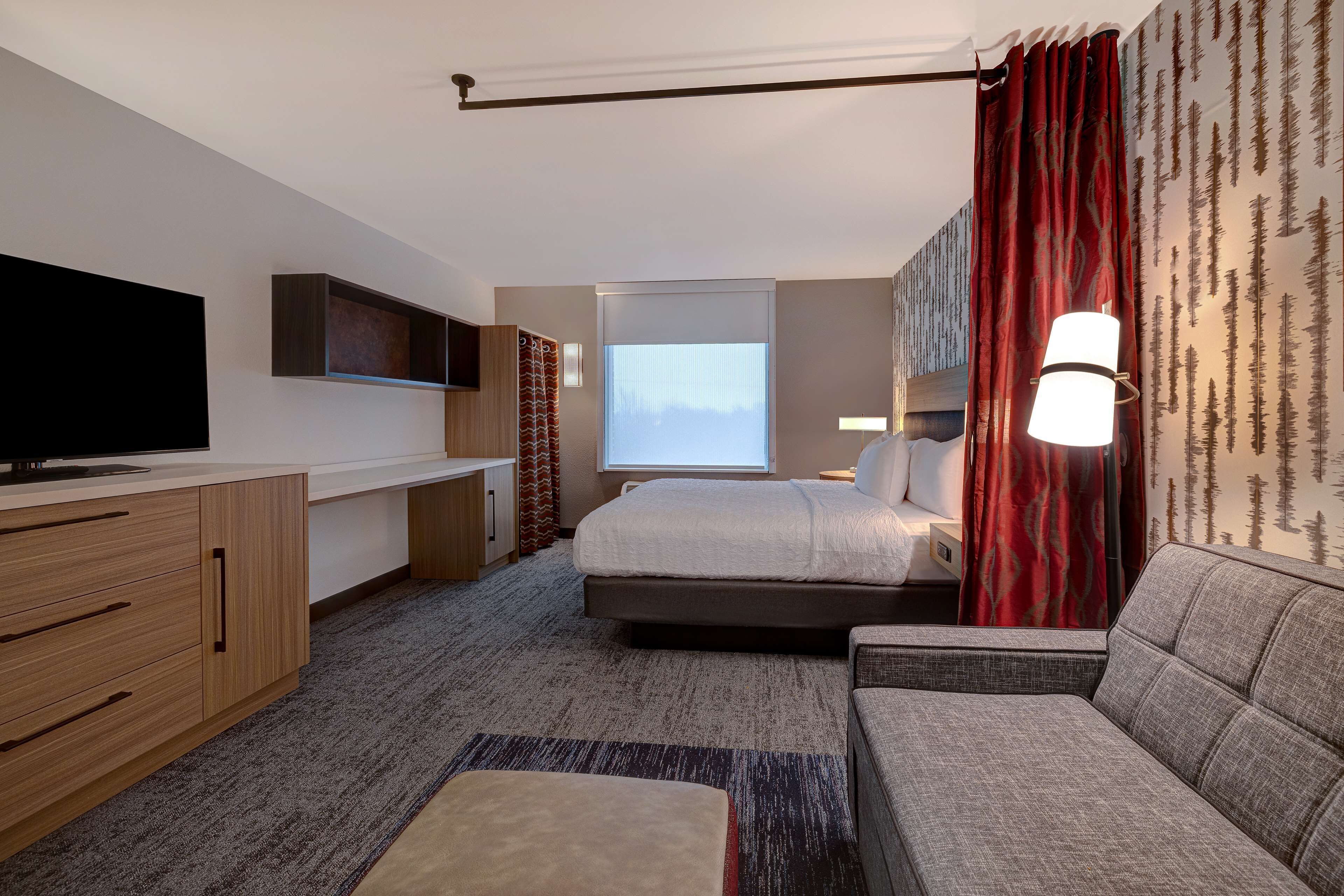 Ein modernes Hotelzimmer mit Bett, Sofa, Fernseher, Schreibtisch und einem Fenster mit Vorhängen.