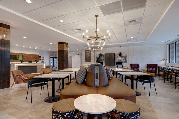 A modern hotel lobby with a central seating area, multiple tables, and a reception desk.