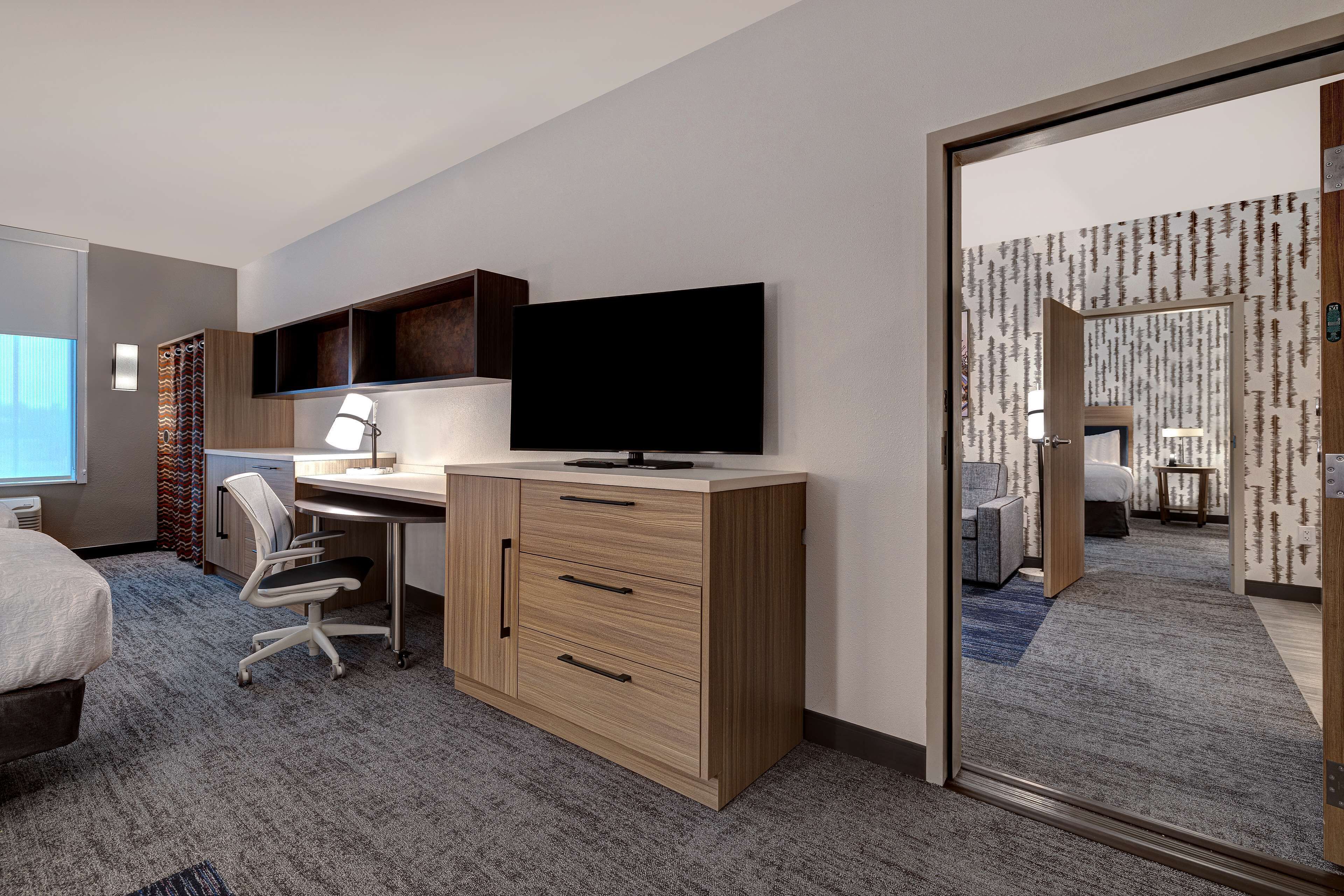 A hotel room with a bed, desk, chair, TV, and a mirror reflecting the room.